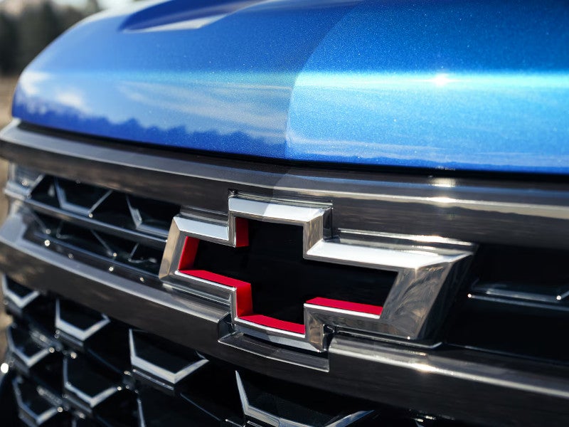 Close-up of the chrome Chevy bowtie emblem with red accents on the front grille of a blue 2026 Chevrolet Silverado 1500.