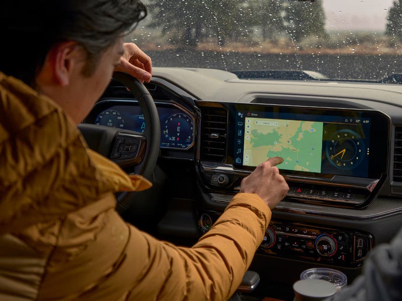 Driver using the large center touchscreen navigation display inside the 2026 Chevrolet Silverado 1500 on a rainy day.