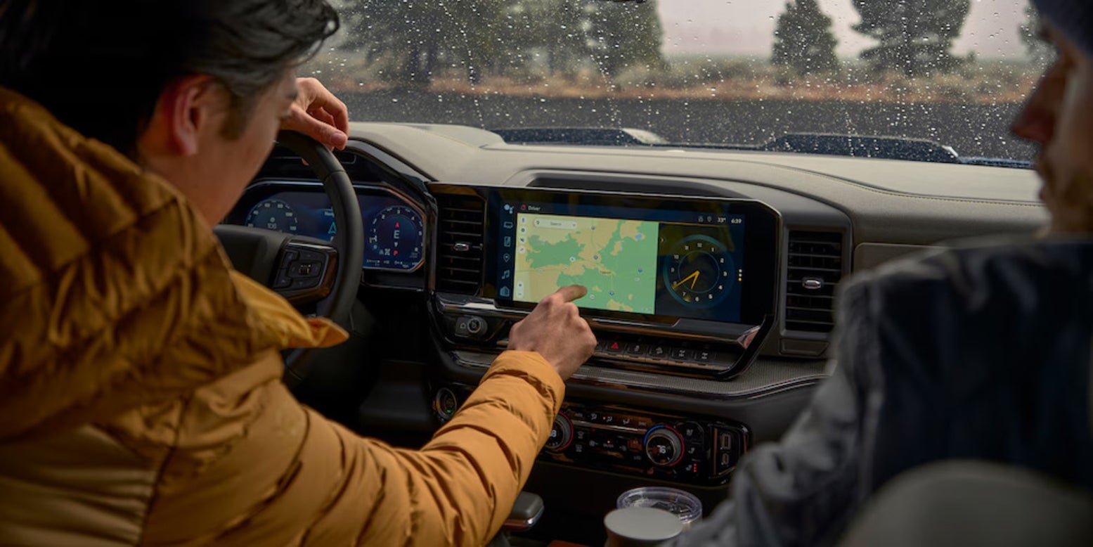 A person in a yellow jacket using the touch screen of the 2026 Chevrolet Silverado